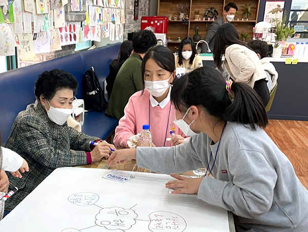 '책 이야기'에 초대된 어르신이 학생들과 함께 그림을 그려가며 대화하고 있다.
