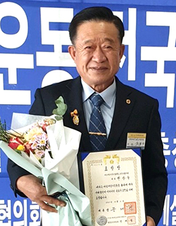 대통령상을 수상한 전광수 회장이 상장과 축하화환을 들고 환하게 웃고 있다.