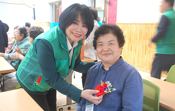 보은군직장새마을회 회원인 가수 박지숙이 어르신께 카네이션을 달아드리고 있다.